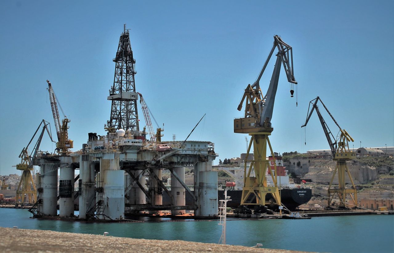 Drilling rig and cranes at dock under blue sky